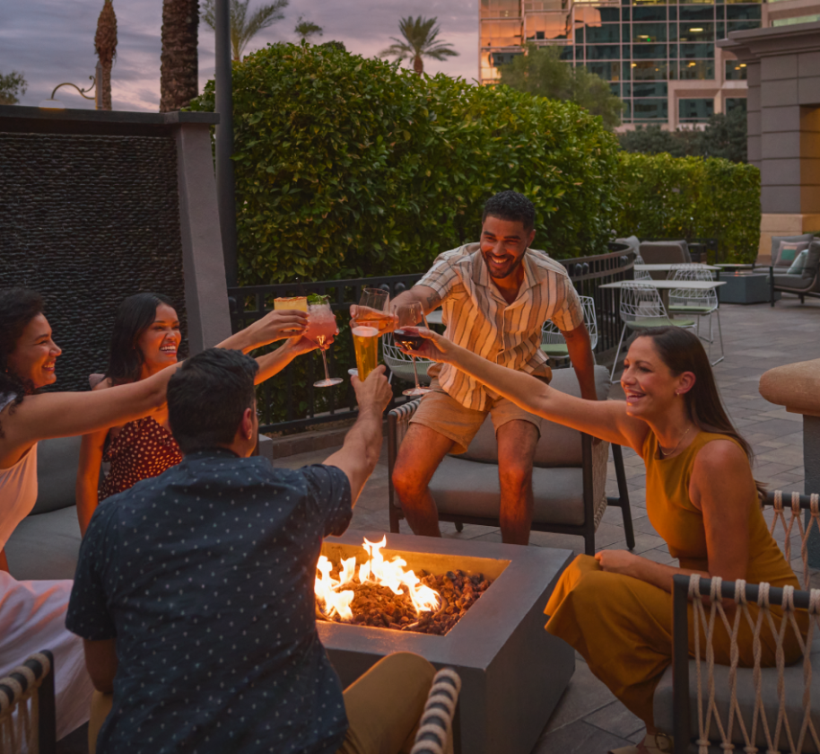 A group of people outside a fire pit having drinks at the Camby