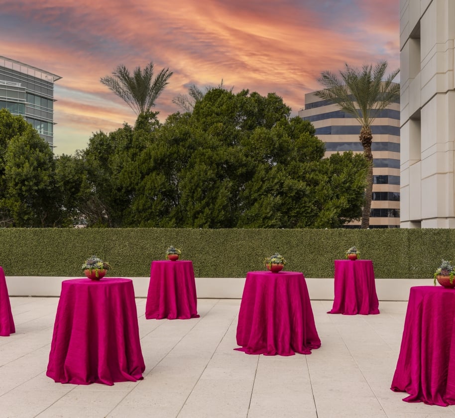 Outdoor space at sunset at the Camby with 6 round standing tables covered in pink table cloths