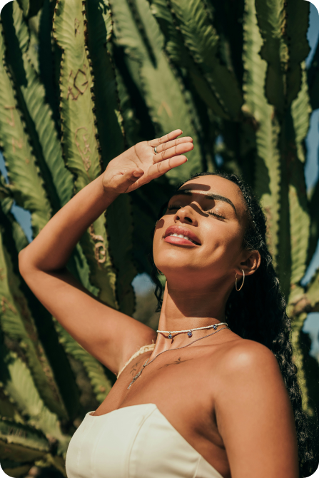 A woman standing beside a large green plant blocking out the sun with her hand in Phoenix