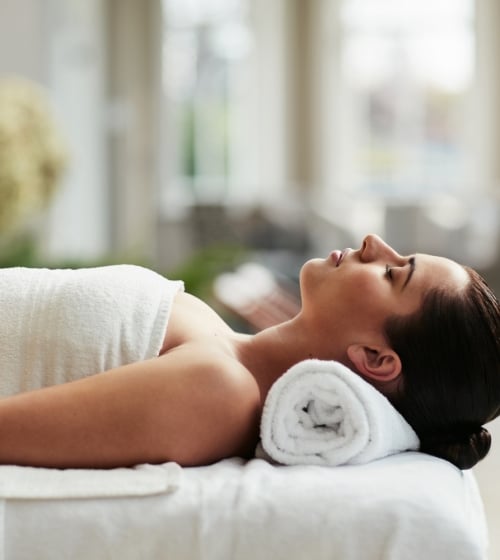 A woman laying on her back with. towel roll under her neck at Aji Spa