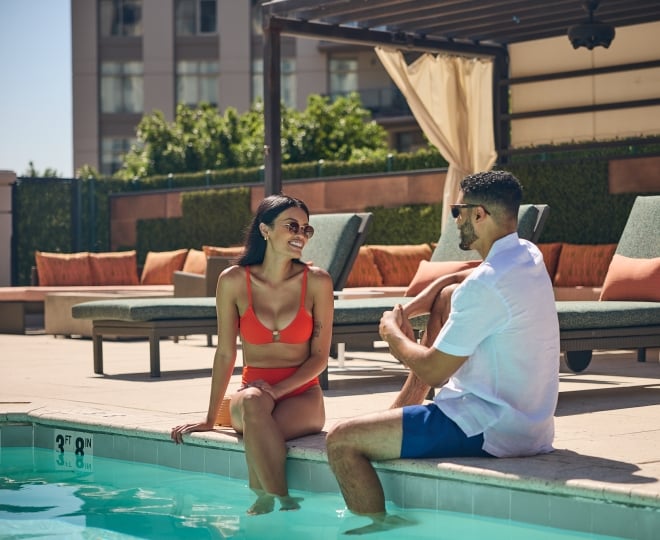 A man and a woman sitting on the edge of the rooftop pool at the Camby