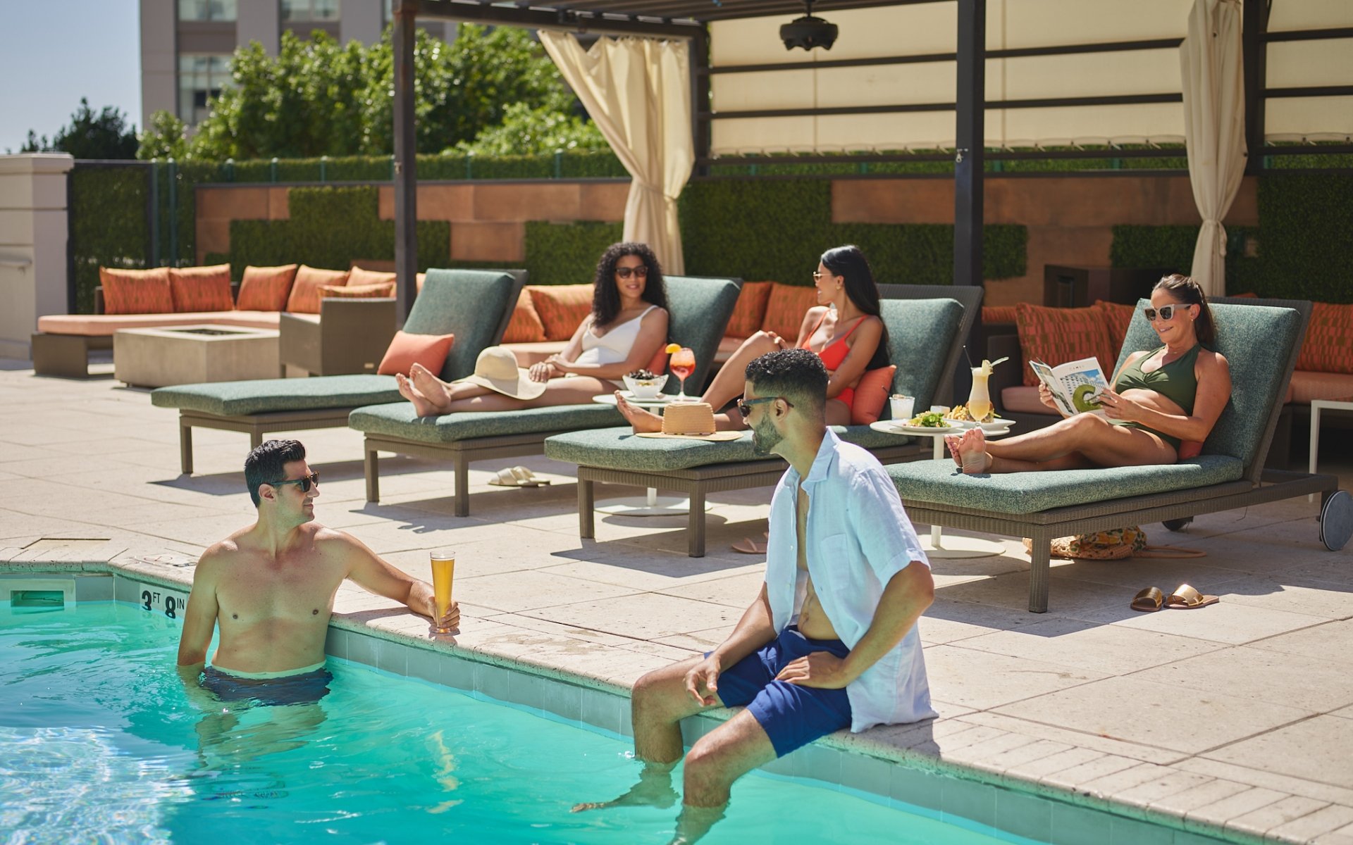 3 women lounging and 2 men hanging poolside at the Camby